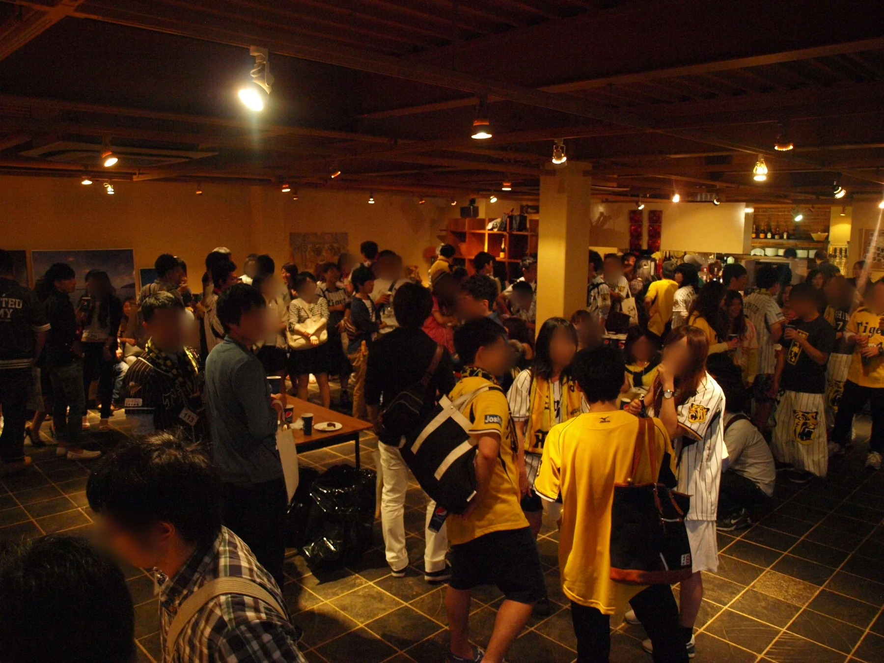 阪神タイガースのファンらしき人々が屋内のイベント会場に集まり、交流を楽しんでいる様子