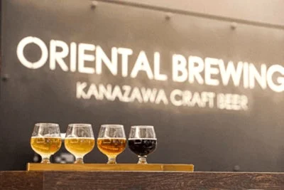 「ORIENTAL BREWING KANAZAWA CRAFT BEER」の看板を背景に、4種類のクラフトビールが並べられたテイスティングセット